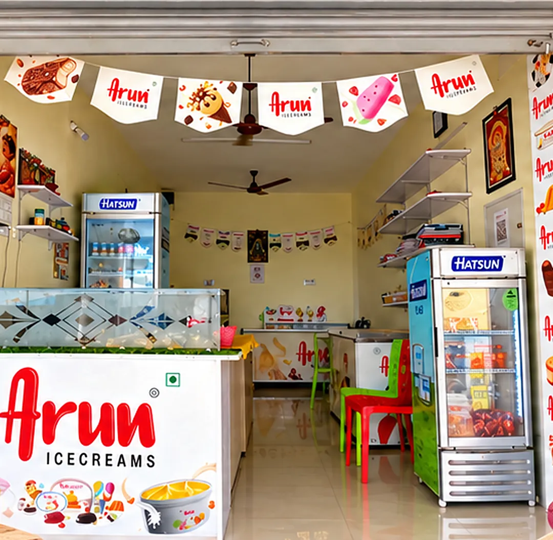 Inside Aruvi: an ice cream counter with Arun Icecreams branding, two Hatsun freezers, shelves and red and green chairs
